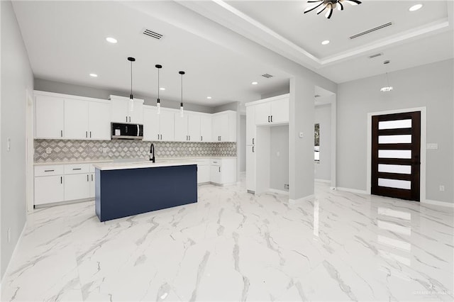 kitchen featuring tasteful backsplash, white cabinetry, an island with sink, and decorative light fixtures