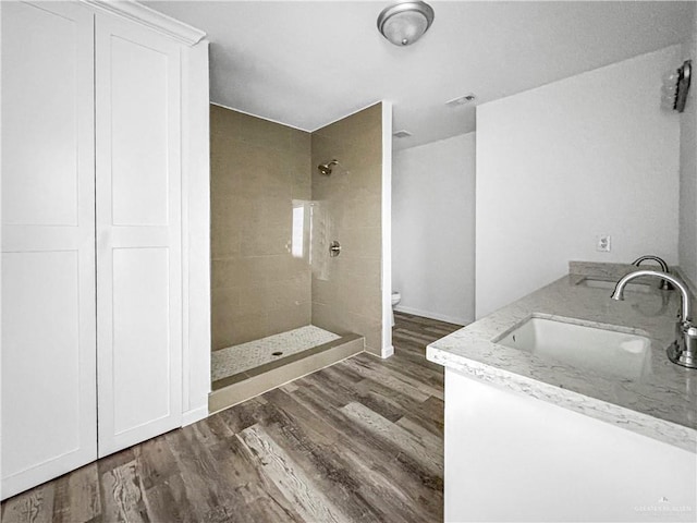 bathroom featuring a tile shower, toilet, vanity, and hardwood / wood-style flooring