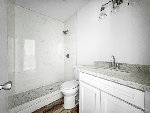 bathroom featuring vanity, toilet, wood-type flooring, and tiled shower