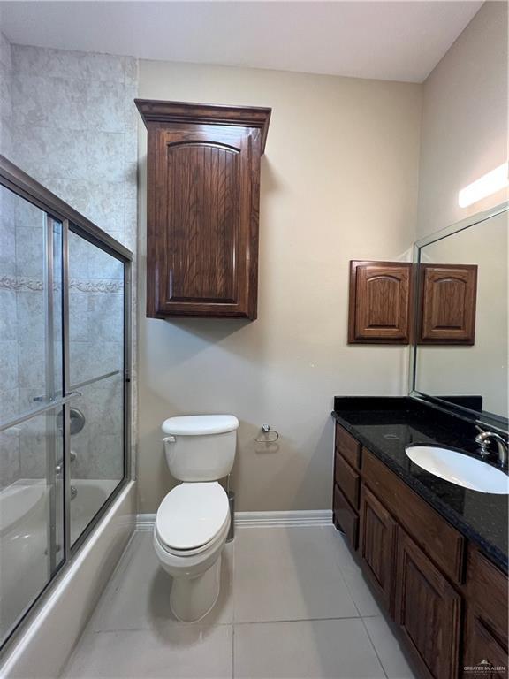 full bathroom with baseboards, toilet, tile patterned flooring, combined bath / shower with glass door, and vanity