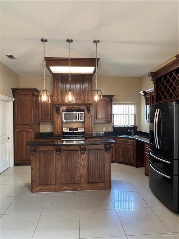 kitchen featuring stainless steel appliances, dark countertops, pendant lighting, and light tile patterned floors