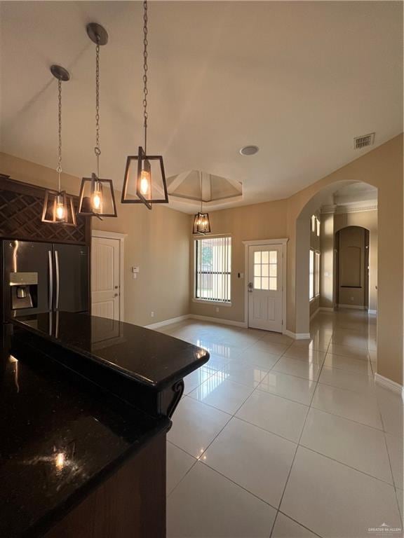 kitchen with arched walkways, light tile patterned floors, hanging light fixtures, stainless steel refrigerator with ice dispenser, and dark countertops