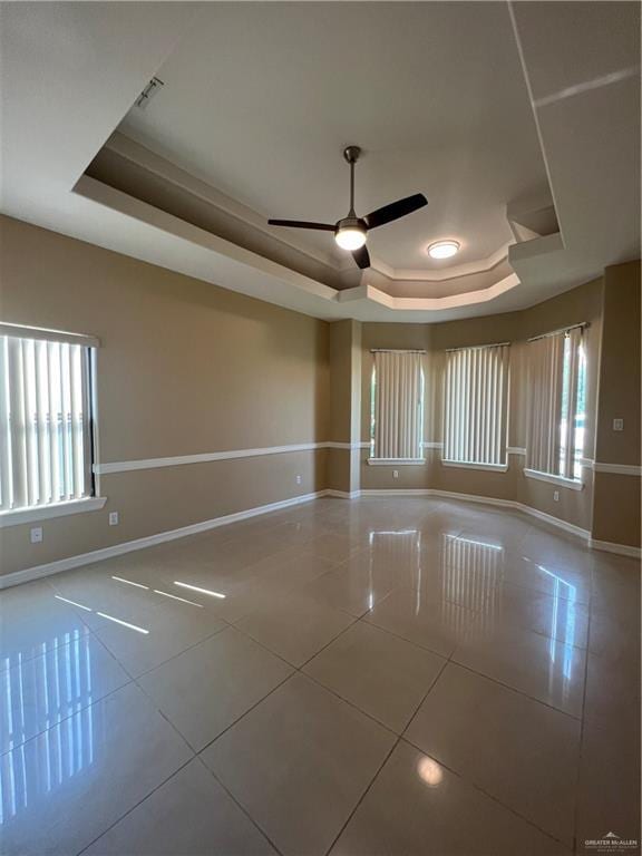 spare room with a ceiling fan, a tray ceiling, baseboards, and tile patterned floors