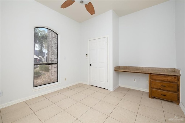 empty room featuring ceiling fan, light tile patterned flooring, and built in desk