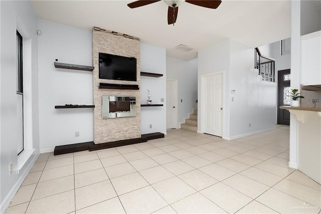 unfurnished living room featuring ceiling fan, light tile patterned floors, and a stone fireplace