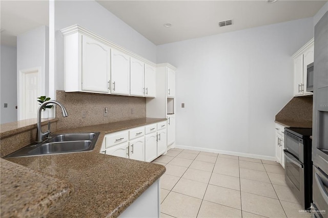 kitchen featuring white cabinetry, decorative backsplash, light tile patterned flooring, dark stone counters, and sink