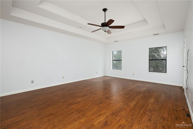 empty room featuring ceiling fan, a tray ceiling, and dark hardwood / wood-style flooring