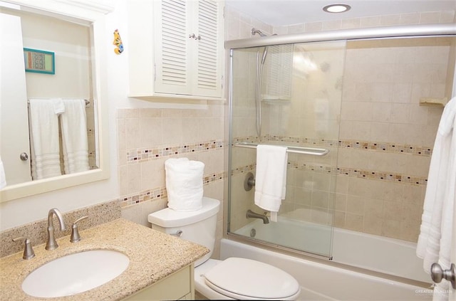 full bathroom with vanity, toilet, bath / shower combo with glass door, and tile walls