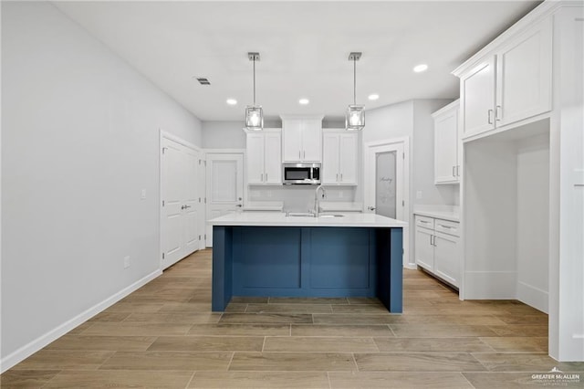 kitchen featuring an island with sink, sink, pendant lighting, and white cabinets