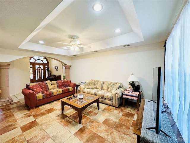 living room featuring a tray ceiling, ornate columns, and ceiling fan