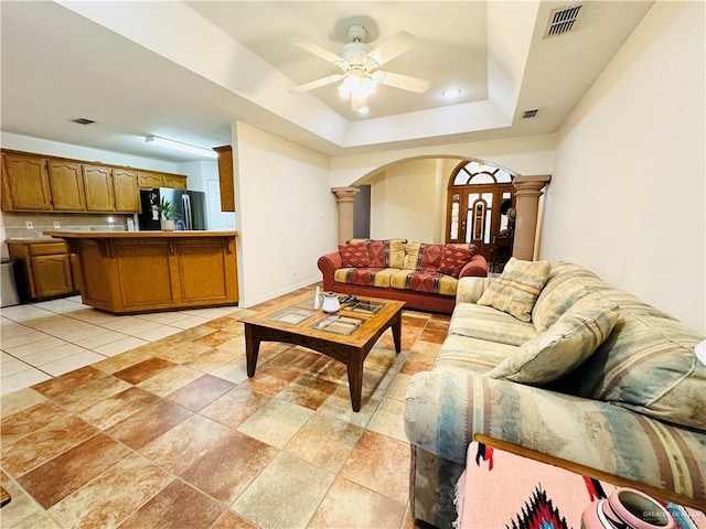 living room with a raised ceiling, ceiling fan, and ornate columns