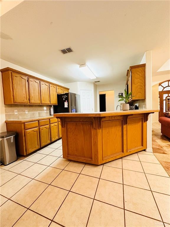 kitchen with stainless steel refrigerator, kitchen peninsula, light tile patterned floors, and a breakfast bar area