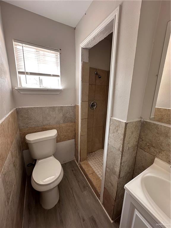 bathroom with a tile shower, vanity, wood-type flooring, tile walls, and toilet