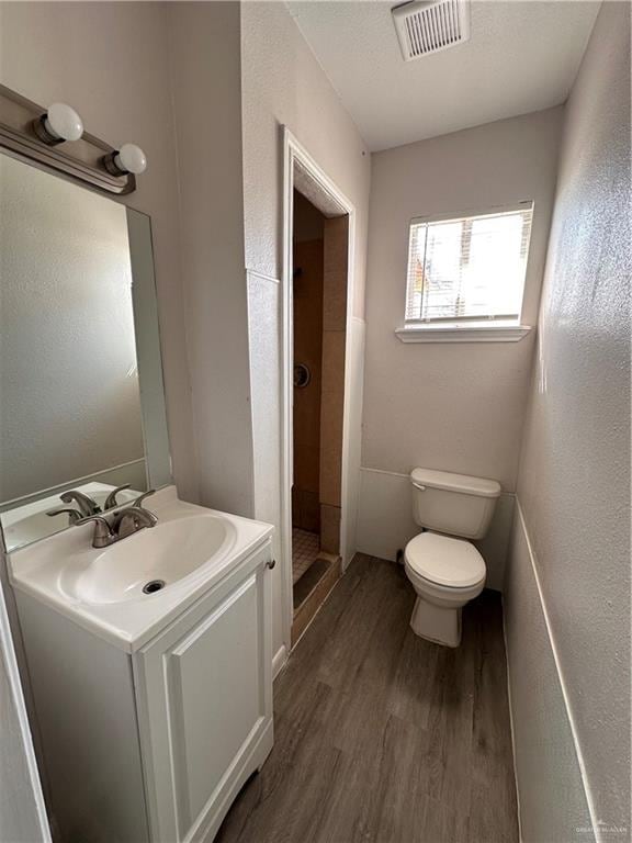 bathroom with hardwood / wood-style flooring, toilet, vanity, and walk in shower