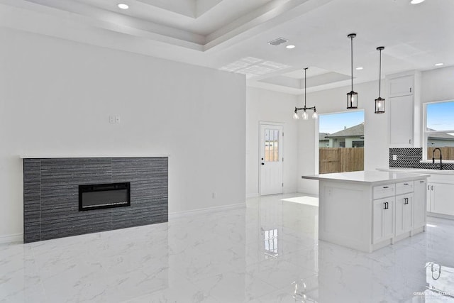 kitchen with a center island, tasteful backsplash, a tray ceiling, white cabinets, and decorative light fixtures