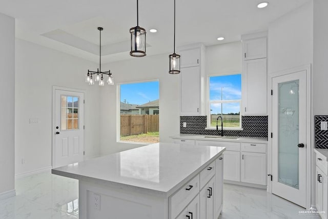 kitchen with sink, hanging light fixtures, tasteful backsplash, white cabinets, and a kitchen island