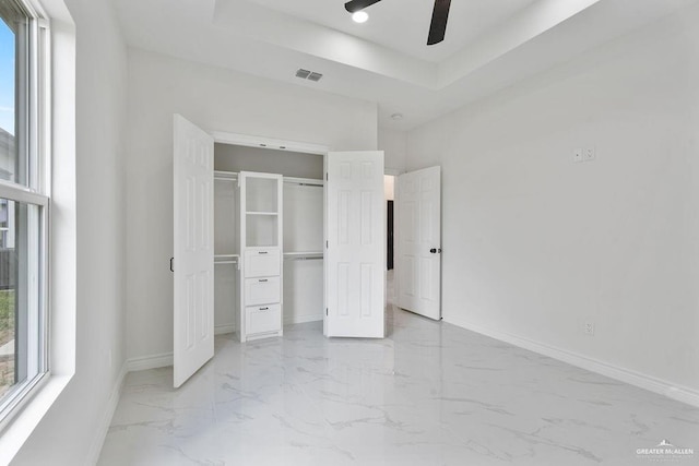 unfurnished bedroom featuring multiple windows, a tray ceiling, a closet, and ceiling fan