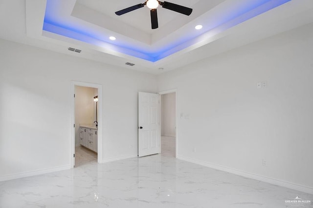 unfurnished bedroom featuring a tray ceiling, ensuite bath, ceiling fan, and a high ceiling