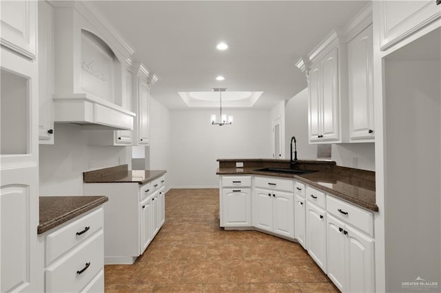 kitchen with pendant lighting, sink, white cabinets, a raised ceiling, and an inviting chandelier