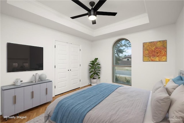 bedroom with a raised ceiling, parquet flooring, ceiling fan, and a closet