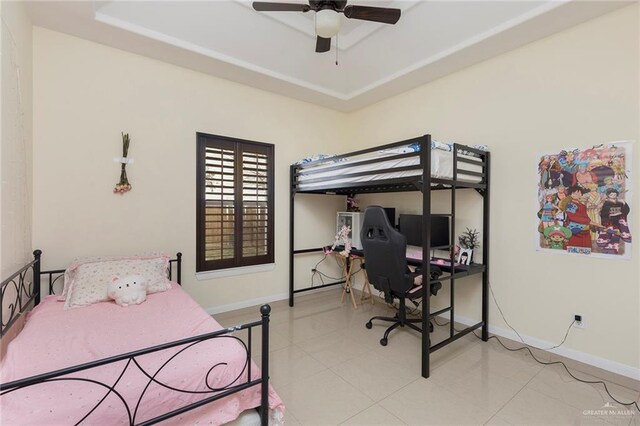 bedroom featuring a raised ceiling, light tile patterned flooring, ceiling fan, and baseboards