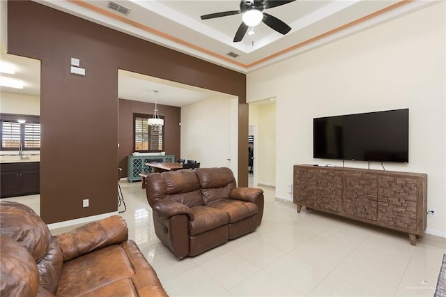 living room with light tile patterned floors, a ceiling fan, visible vents, baseboards, and a tray ceiling