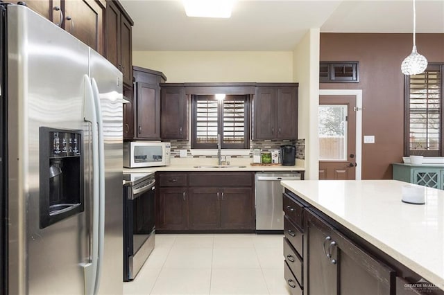 kitchen with stainless steel appliances, a sink, light countertops, decorative backsplash, and decorative light fixtures