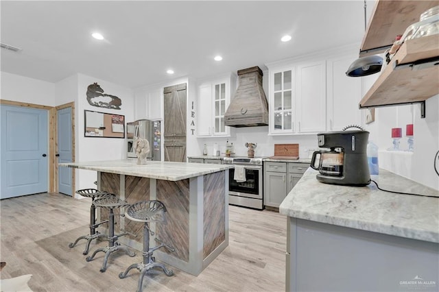 kitchen with appliances with stainless steel finishes, light wood-style floors, light stone countertops, premium range hood, and a kitchen bar