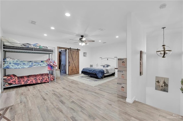 bedroom with a barn door, recessed lighting, visible vents, light wood-style flooring, and ceiling fan with notable chandelier