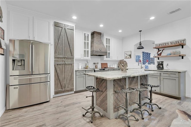 kitchen with light wood finished floors, stainless steel fridge, a barn door, visible vents, and premium range hood