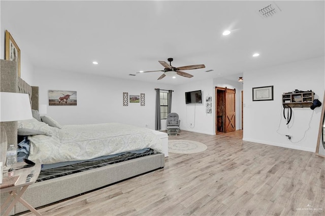 bedroom featuring a barn door, light wood-style flooring, recessed lighting, visible vents, and baseboards