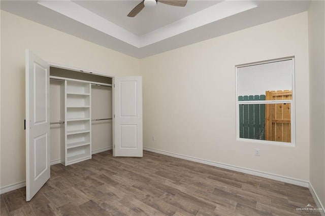 unfurnished bedroom with hardwood / wood-style flooring, ceiling fan, a raised ceiling, and a closet