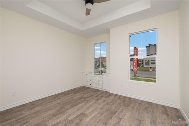 empty room featuring a tray ceiling, ceiling fan, and light wood-type flooring