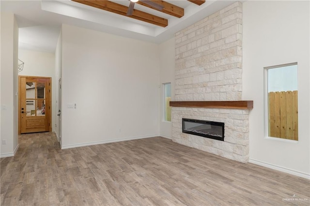 unfurnished living room with beam ceiling, a stone fireplace, a towering ceiling, and light hardwood / wood-style floors