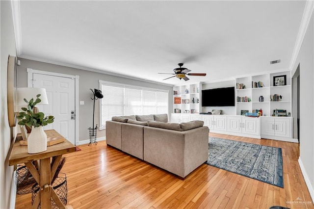 living room with ceiling fan, crown molding, built in features, and light hardwood / wood-style floors