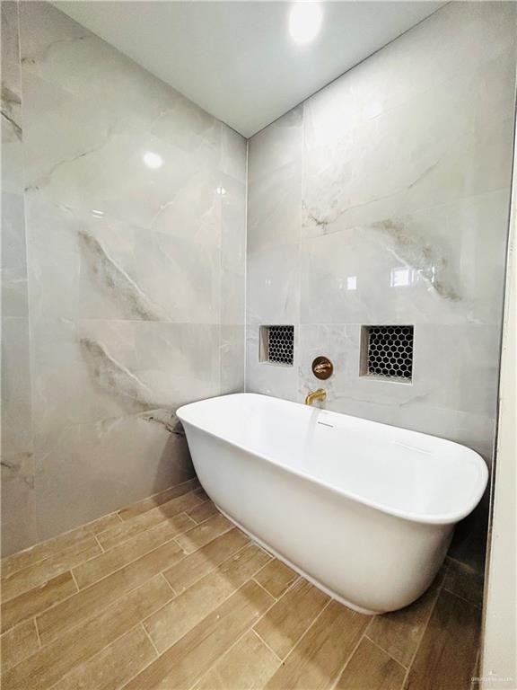 412 S Bowie Ave, Elsa, TX 78538 - full bathroom with tile walls, a freestanding tub, and wood finish floors