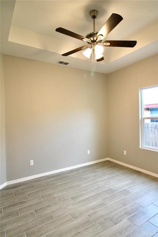 empty room featuring wood tiled floor, visible vents, ceiling fan, and baseboards