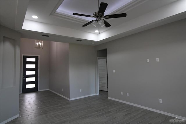 empty room with a tray ceiling, dark wood-style flooring, baseboards, and recessed lighting