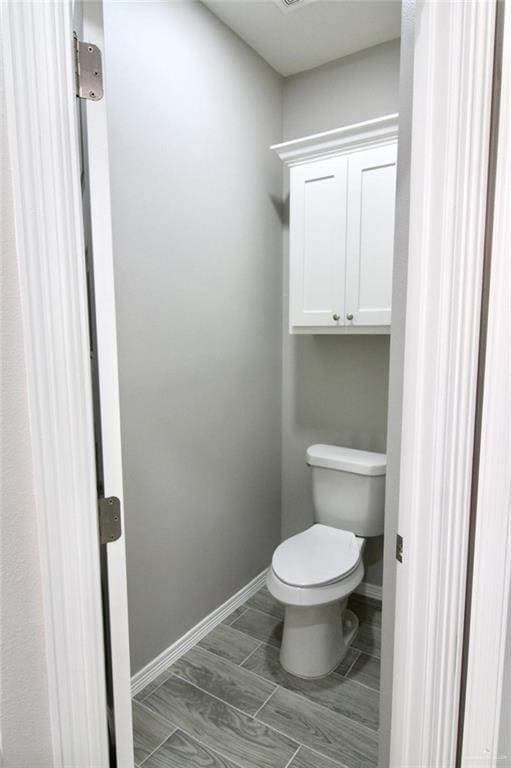 bathroom with toilet, baseboards, and wood finish floors