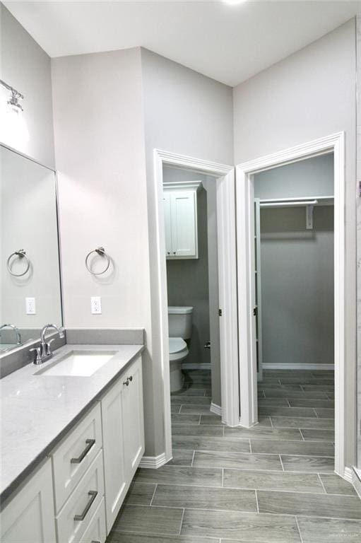 full bath with toilet, wood finish floors, vanity, baseboards, and a spacious closet