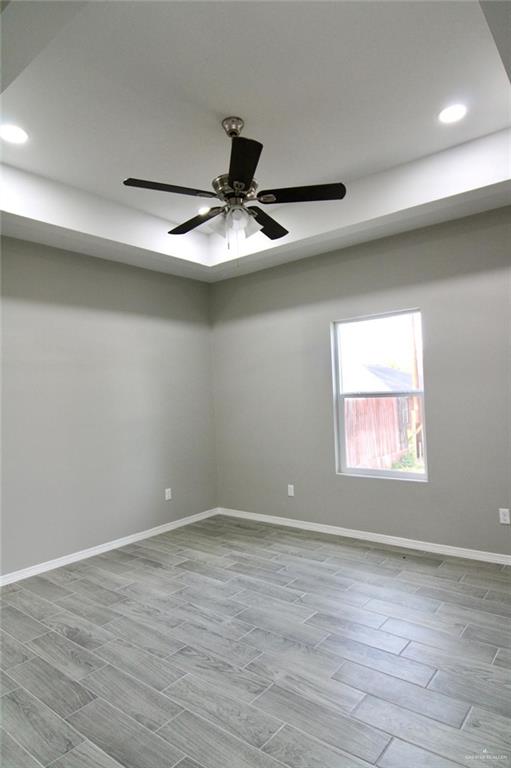 empty room with baseboards, ceiling fan, wood tiled floor, a tray ceiling, and recessed lighting