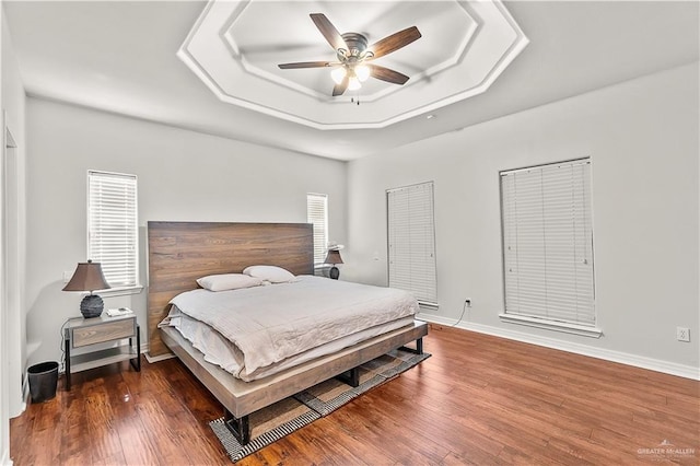 bedroom featuring a raised ceiling, ceiling fan, and dark wood-type flooring