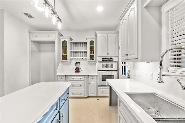 kitchen with white cabinets, sink, hanging light fixtures, light tile patterned floors, and stainless steel double oven