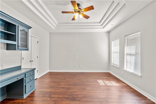 spare room with built in desk, a raised ceiling, ceiling fan, and dark wood-type flooring