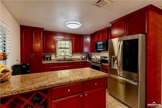 3417 Belinda St, Edinburg, TX 78541 - kitchen with stainless steel appliances, dark brown cabinets, light tile patterned floors, light stone countertops, and red cabinets