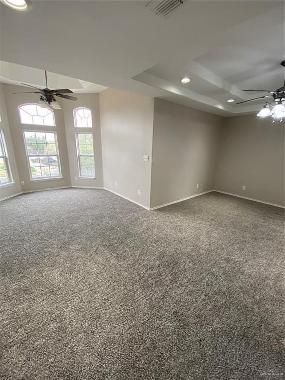 carpeted spare room with a raised ceiling and ceiling fan