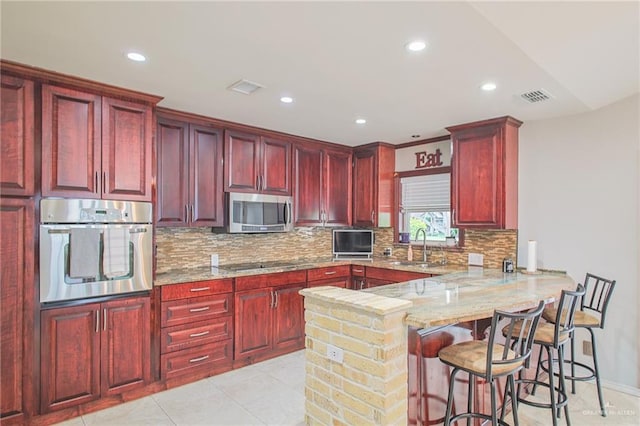 kitchen with stainless steel appliances, light stone counters, kitchen peninsula, a kitchen bar, and light tile patterned floors