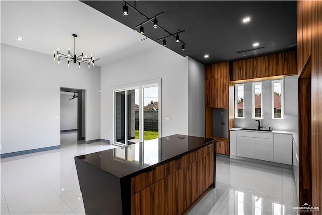 kitchen featuring ceiling fan with notable chandelier, a spacious island, sink, hanging light fixtures, and light tile patterned floors