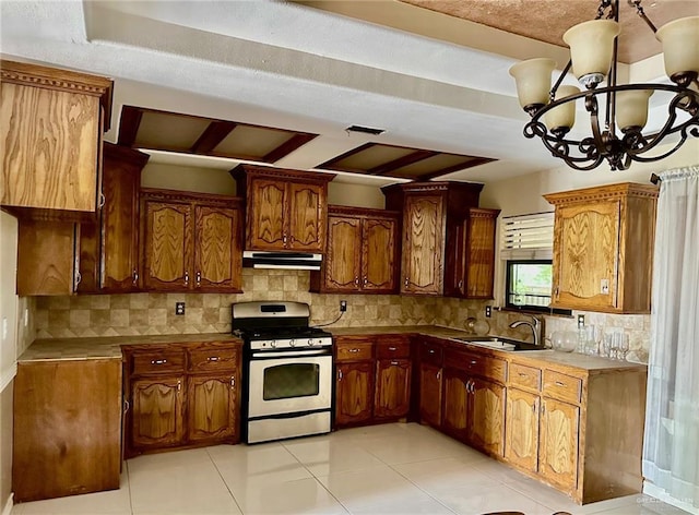 kitchen with stainless steel range with gas cooktop, sink, decorative backsplash, light tile patterned floors, and a chandelier