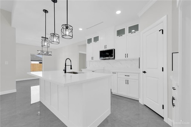 kitchen featuring stainless steel microwave, white cabinets, a kitchen island with sink, and a sink